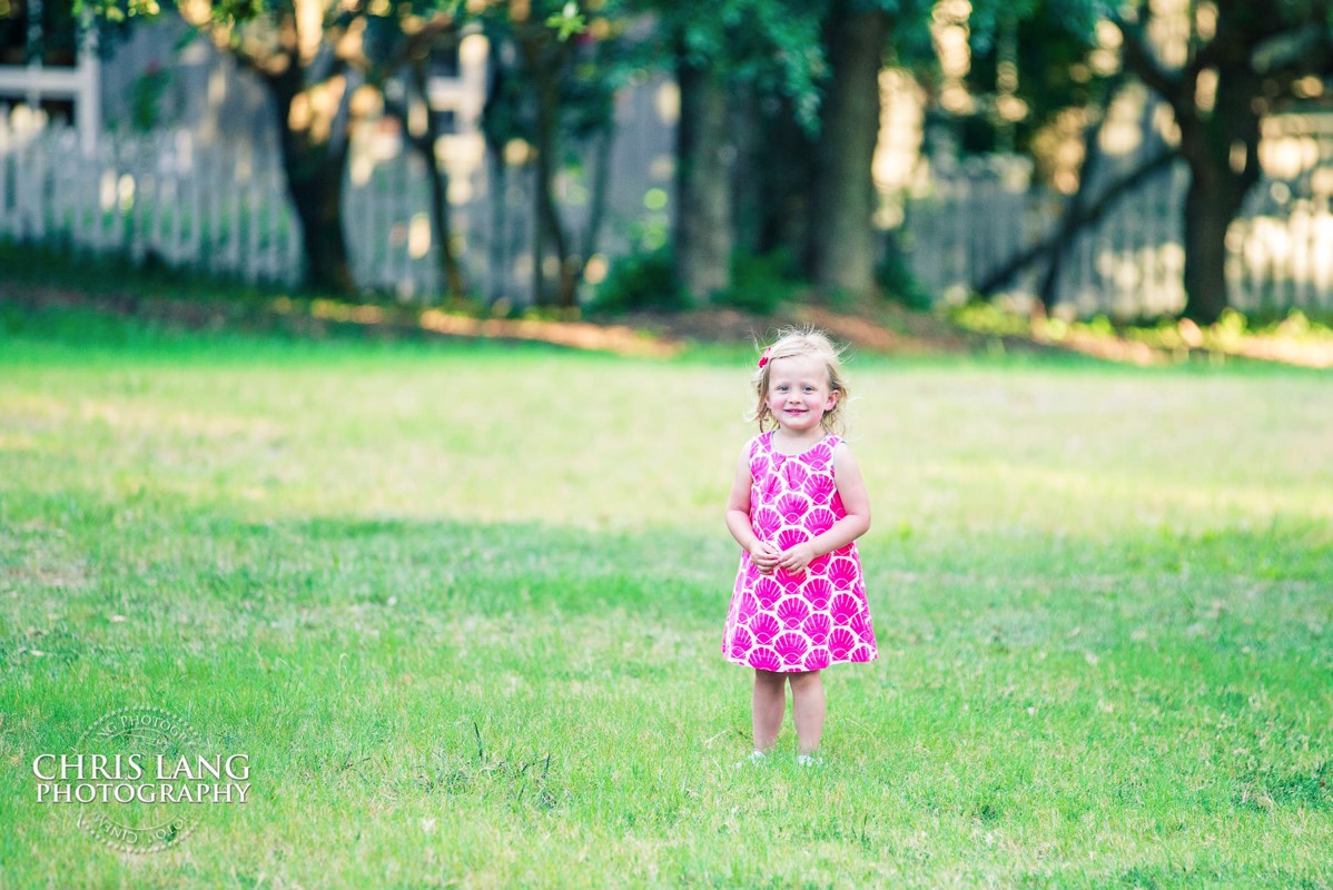 little girl standing in a field - pink dress - pink ribbon in hair - Places for family vacation - Bald Head Island Photographers - BHI Photography - Kids Portraits -  Pictures on Bald Head Island - BHI Photo Services - Chris Lang Photography 
