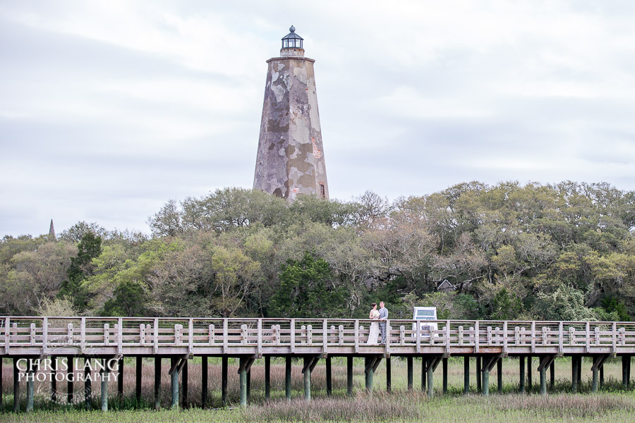 Wedding picture of bride and groom on the wood bridge with Old Baldy lighthouse in the background - Bald Head Island NC Weddings - Photographers - Bride - Groom - Wedding Dress - wedding photography - chris lang photography - destination wedding - Bald Head Island Wedding Venue 