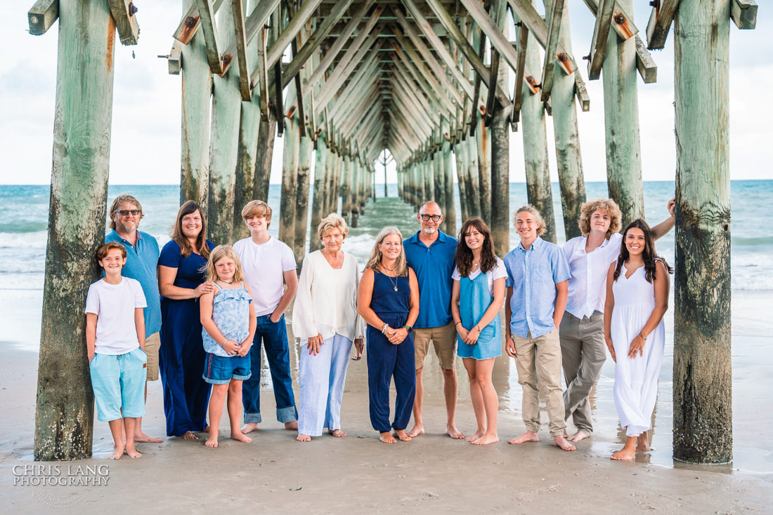 Family posing for picture under the Surf City Pier  - ocean waves -Topsail Island Photography - Topsail Island NC Photographers - Chris Lang Photography -  Beach Photography - Family Photographer - Family photo - Beach Photographer - Beach Portraits -  Coastal Lifestyle Photography