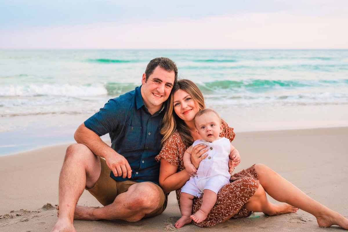 Image of young couple with thier infnat sittong on the beach - Beach portraits -Wrightsville Beach Family Photography - Wrightsville Beach Photographers - Beach Family Photos- Chris Lang Photography  