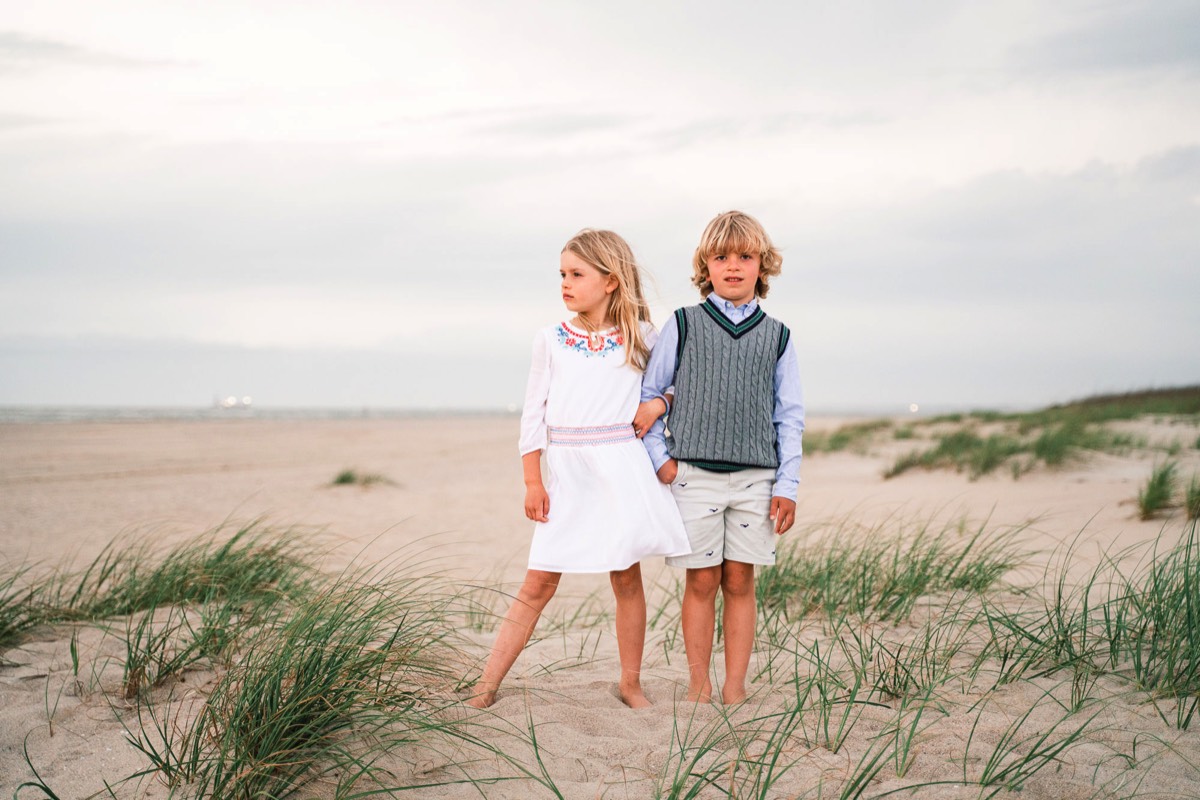 Image of brother and sister posing for beach photo - shorts and sweather vest - white sun gress - Wrightsville Beach Family Photography - Wrightsville Beach Photographers - Beach Family Photos- Chris Lang Photography  