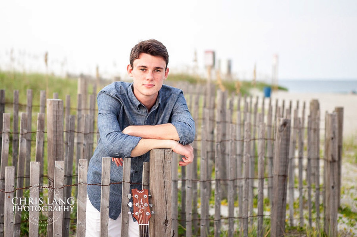 image of  high school senior boy posing on beach fence - senior portriat ideas - Wrightsville Beach High School Senior Photography - Wrightsville Beach Photographers - Beach Senior Portrait  Photos- Chris Lang Photography  