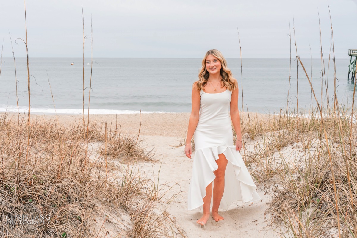 image of highschool senior girl walking up the beach path in a white fress - senior photo idea - Wrightsville Beach High School Senior Photography - Wrightsville Beach Photographers - Beach Senior Portrait  Photos- Chris Lang Photography  