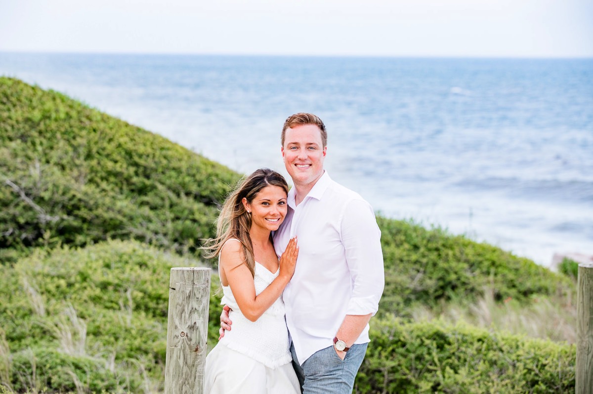 Engagement photo of couple with ocean in the background -  white sundress - Fort Fisher North Carolina -  Engagement Photography - Wedding Ideas - Popular engagement location - Lifestyle engagement photo -  Ft Fisher engagement photographers - Engagement session ideas - Chris Lang Photography